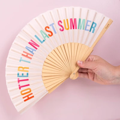 Abbildung von Fisura Handfächer aus Holz mit der Aufschrift Hotter Than Last Summer“. Trendiges, farbenfrohes Accessoire, tragbarer beigefarbener Handventilator Aufhänger. Maße: 42,5 x 23 cm