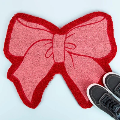 Abbildung von Fisura Originelle Kokosfußmatte Rosa Schleife“ mit Rutschfester PVC Unterseite. und rote Türmatte in Schleifenform. Maße: 58,5 cm x 50 cm.