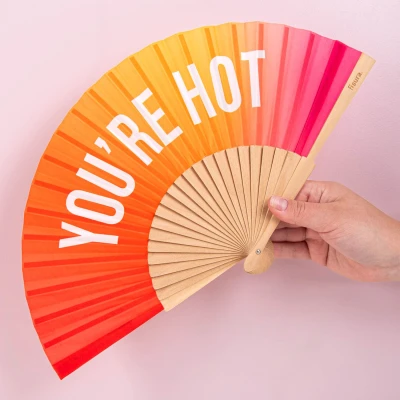 Abbildung von Fisura Handfächer aus Holz mit der Aufschrift You Are h*t“. Modernes, farbenfrohes Accessoire rosa orangefarbenem Farbverlauf, tragbarer Ventilator Aufhänger. Maße: 42,5 x 23 cm